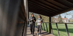 Middle-aged couple walking energetically through a sunlit park, revitalized and healthy, with a wellness center in the distance